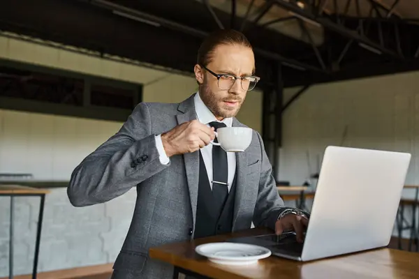 Konzentrierter Geschäftsmann mit Brille und Krawatte im schicken Anzug beim Teetrinken am Laptop — Stockfoto