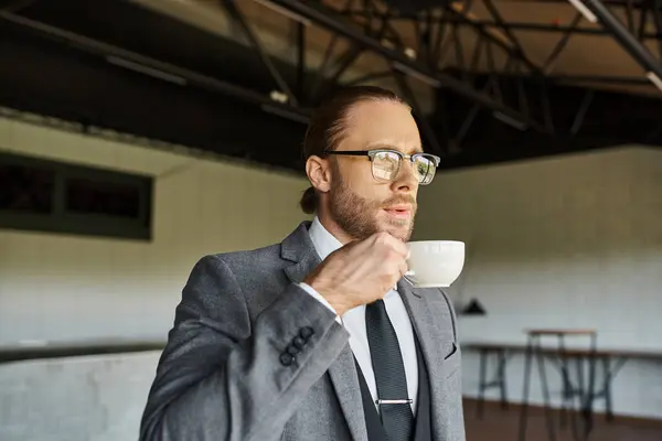 Schöner, raffinierter Profi mit Brille und Pferdeschwanz im schicken Anzug, der Tee trinkt und wegschaut — Stockfoto