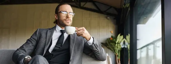 Красивый привлекательный мужчина в сером умном костюме пьет чай и смотрит в сторону, бизнес-концепция, баннер — стоковое фото