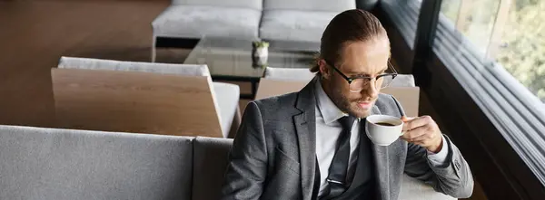 Красивий чоловік в розумному шикарному костюмі в окулярах п'є теплий чай на дивані, бізнес-концепція, банер — стокове фото