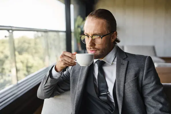 Bel homme avec costume de style dapper avec lunettes et cravate boire du thé sur le canapé, concept d'affaires — Photo de stock