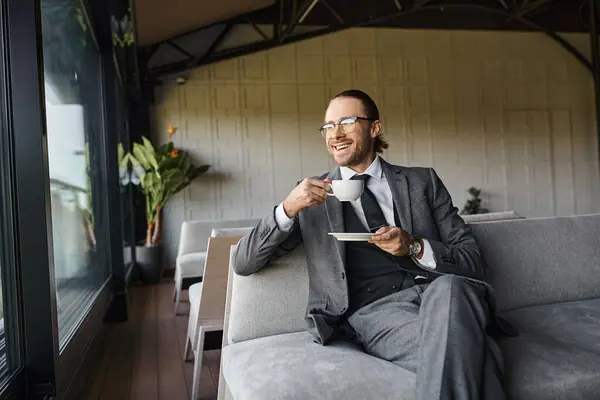 Bom olhar alegre profissional em terno cinza sentado no sofá e beber chá, conceito de negócio — Fotografia de Stock