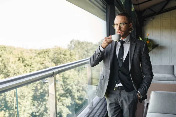 Handsome refined man in gray suit with glasses drinking tea with hand in pocket, business concept — Stock Photo