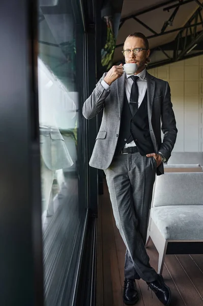 Ansprechender Profi im schicken Anzug mit Gläsern, die Tee mit der Hand in der Tasche trinken, Geschäftskonzept — Stockfoto
