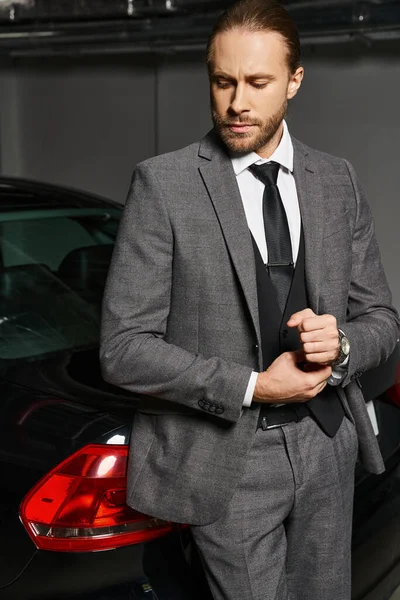 Good looking elegant businessman with red hair in smart suit posing next to his car on parking lot — Stock Photo