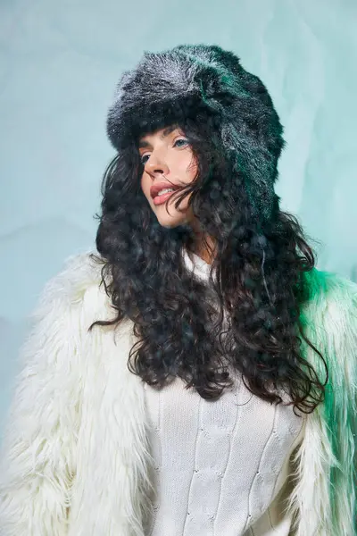 Cheerful young woman with furry hat and white attire smiling on grey backdrop, winter fashion — Stock Photo