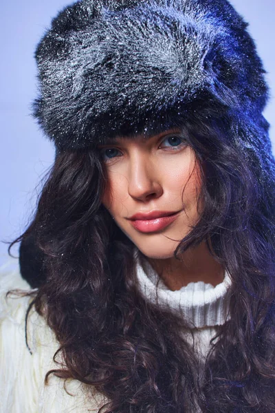 Bellezza invernale, giovane donna dagli occhi azzurri in posa in cappello con neve su sfondo grigio, aria fresca — Foto stock