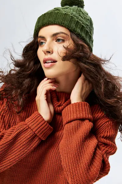 Привлекательная женщина в шляпе с помпоном и вязаными терракотовыми свитерами позирует на сером фоне — стоковое фото
