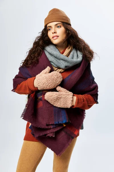 Cozy layers, brunette woman in layered clothes with warm scarf and mittens on grey backdrop — Stock Photo