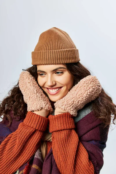 Winter fashion, pleased young woman in layered clothes with warm scarf and mittens on grey backdrop — Stock Photo