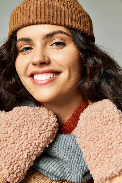 Wintermodekonzept, glückliche junge Frau mit Strickmütze und Fäustlingen, die vor grauem Hintergrund lächeln — Stockfoto