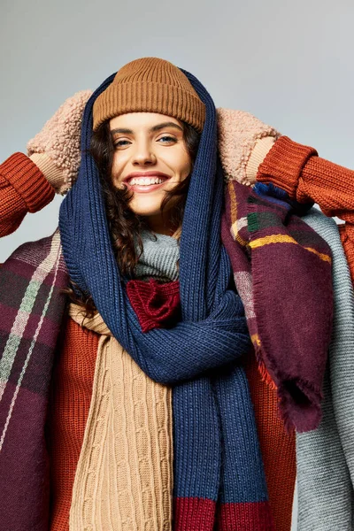 Winter fashion, positive woman in layered clothing, knitted hat and scarfs posing on grey backdrop — Stock Photo