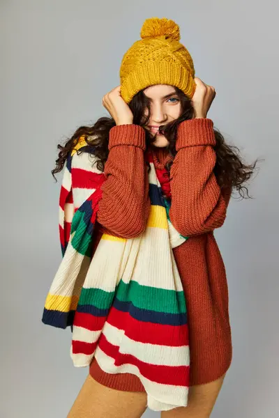 Счастливая женщина в уютной шляпе и свитере с раздетым шарфом, позирующая на сером фоне — стоковое фото