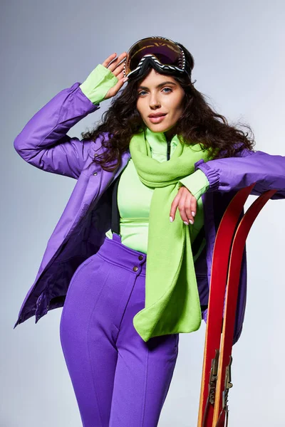 Winter activity, attractive woman with curly hair posing in active wear with puffer jacket and skis — Stock Photo