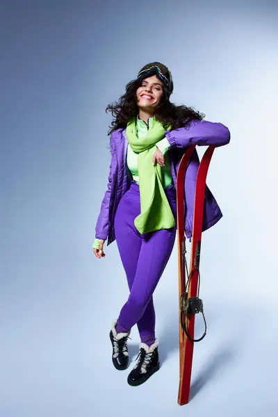 Activité d'hiver, femme satisfaite avec les cheveux bouclés posant en tenue active avec veste gonflante et skis — Photo de stock