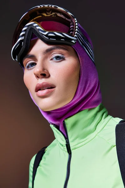Hermosa mujer en ropa de esquí de invierno con pasamontañas en la cabeza mirando a la cámara en el fondo gris oscuro - foto de stock