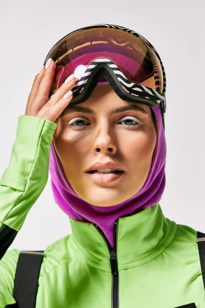 Молода жінка в зимовому лижному одязі з балаклавою на голові дивиться на камеру на сірому фоні — стокове фото