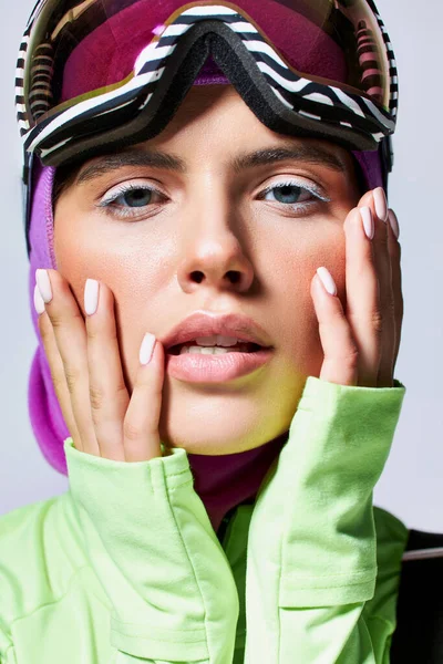 Retrato de mulher bonita em roupas de esqui de inverno com balaclava na cabeça tocando rosto em cinza — Fotografia de Stock