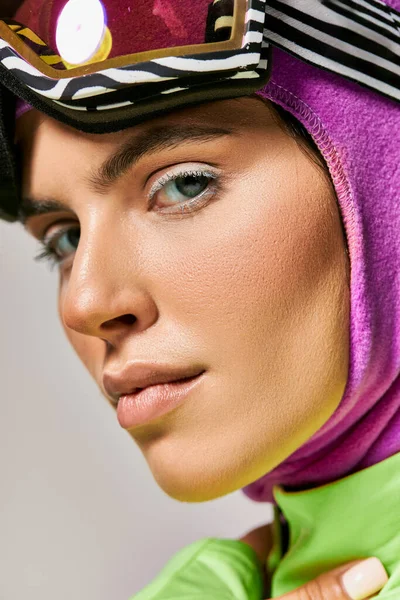 Primer plano de la mujer en ropa de esquí de invierno con pasamontañas en la cabeza mirando a la cámara en gris, retrato - foto de stock