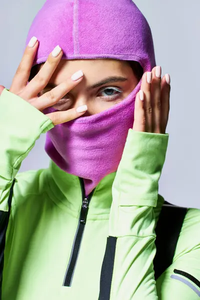 Portrait of woman with blue eyes wearing purple ski mask and looking at camera on grey backdrop — Stock Photo