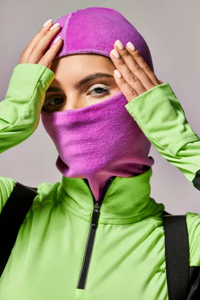 Portrait of woman with blue eyes wearing purple ski mask and looking at camera on grey background — Stock Photo