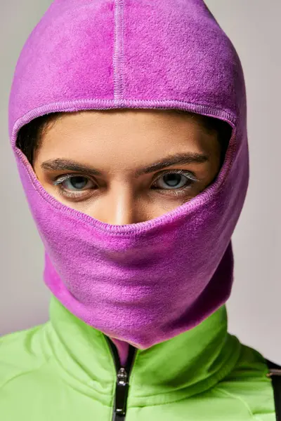 Ritratto di giovane donna con gli occhi azzurri in maschera da sci viola guardando la fotocamera su sfondo grigio — Foto stock