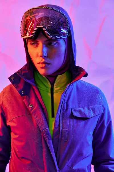 Hermosa mujer en máscara de esquí y googles usando chaqueta caliente sobre fondo púrpura, moda de invierno - foto de stock