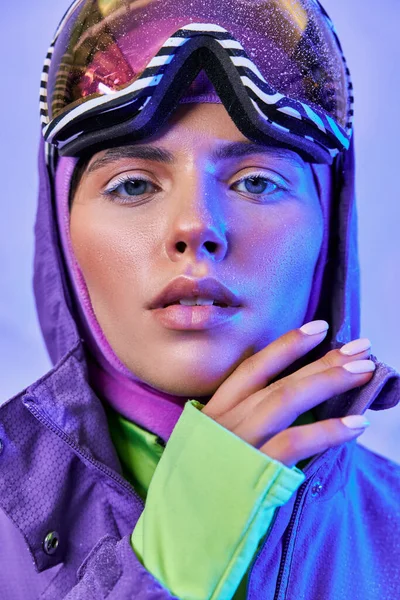 Jovem mulher em máscara de esqui, googles e casaco quente olhando para longe no fundo roxo, beleza de inverno — Fotografia de Stock