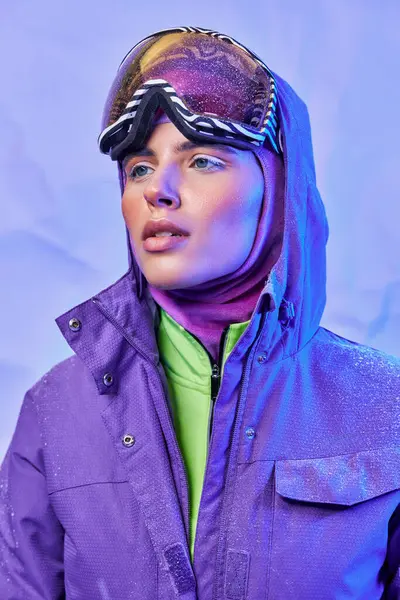 Air d'hiver croustillant, jeune femme en masque de ski, googles et veste chaude regardant loin sur fond violet — Photo de stock