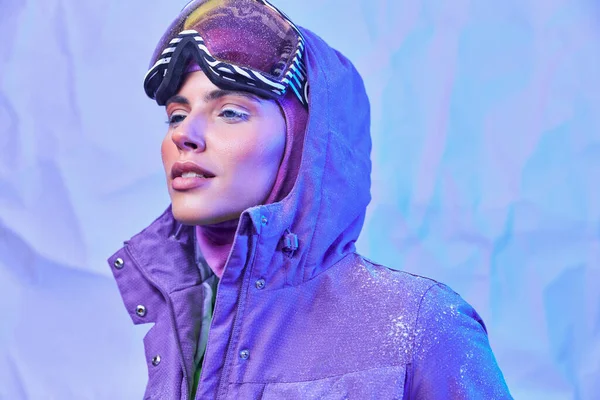 Морозне зимове повітря, молода жінка в лижній масці, окулярах і теплий піджак дивиться на фіолетовий фон — стокове фото