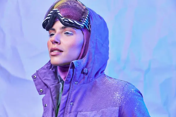Air hivernal givré, jeune femme en masque de ski, googles et veste chaude regardant loin sur fond violet — Photo de stock
