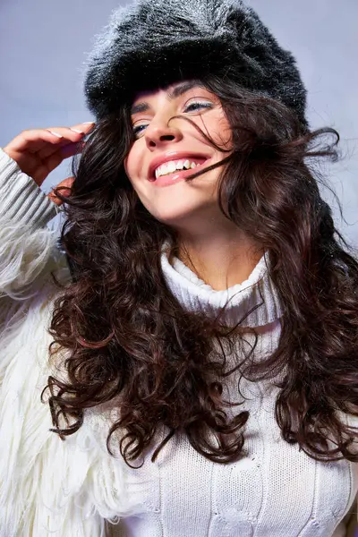 Cheerful woman in white faux fur jacket, hat and sweater posing on grey backdrop, winter fashion — Stock Photo