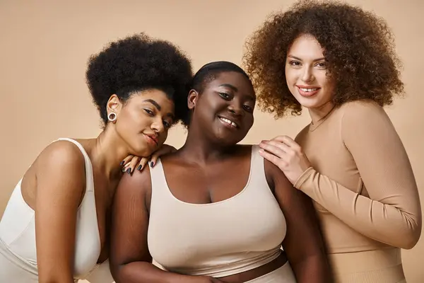 Multiethnic curvy and body positive women in underwear on beige backdrop, natural plus size beauty — Stock Photo