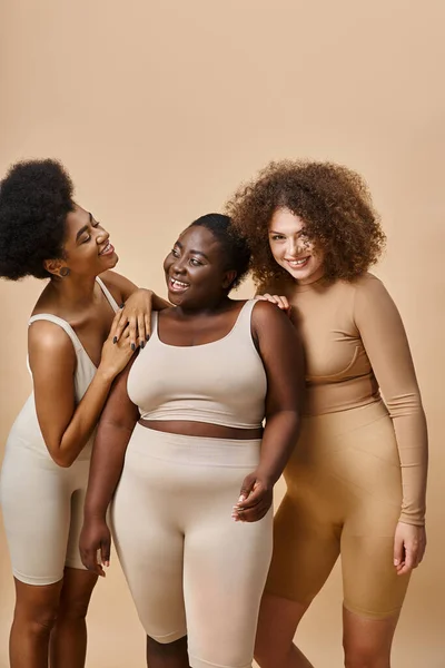 Multiethnic curvy and body positive women in underwear on beige backdrop, natural plus size beauty — Stock Photo