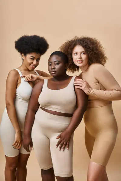 Happy multiracial body positive women in underwear on beige backdrop, natural and curvy beauty — Stock Photo