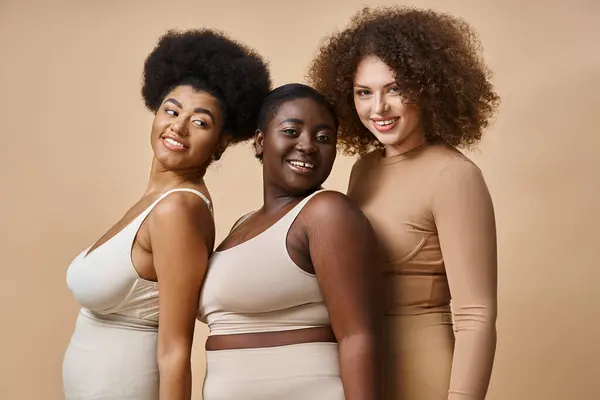 Happy multiracial body positive women in underwear on beige backdrop, natural and curvy beauty — Stock Photo