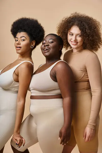 Charming multiethnic plus size women in lingerie smiling at camera on beige backdrop, body positive — Stock Photo