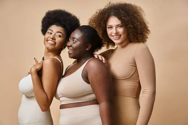 Joyeux multiethnique plus la taille des femmes en sous-vêtements posant sur fond beige, confiance en soi et charme — Photo de stock