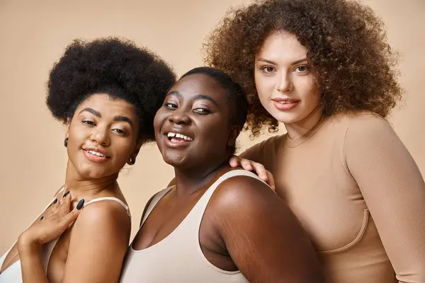 Joyeux multiethnique plus la taille des femmes en sous-vêtements posant sur fond beige, confiance en soi et charme — Photo de stock