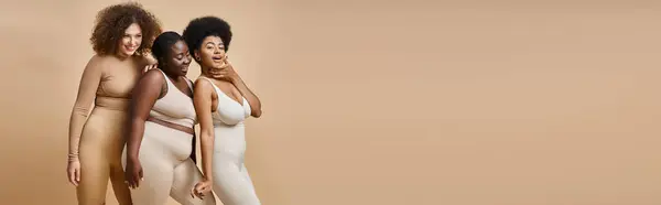 Joyeux multiethnique plus la taille des femmes en sous-vêtements posant sur fond beige, confiance en soi, bannière — Photo de stock