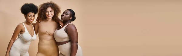 Corpo multietnico donne positive in biancheria intima sorridente su sfondo beige, plus size bellezza, banner — Foto stock