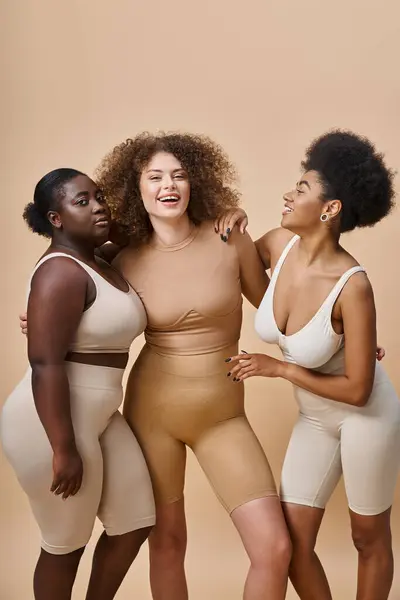 Alegre multiétnico plus size mulheres em lingerie posando em bege, auto-aceitação e beleza — Fotografia de Stock