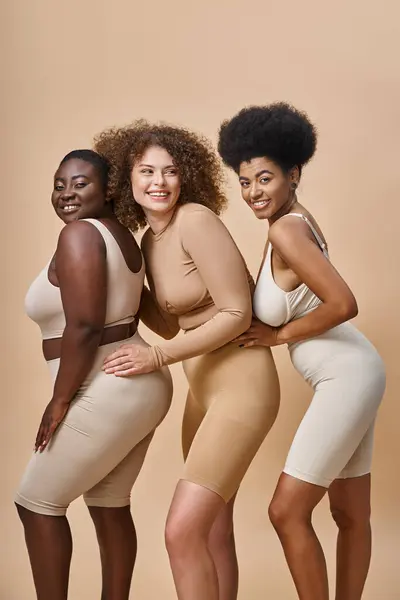 Smiling body positive multiracial women in underwear posing on beige backdrop, plus size charm — Stock Photo