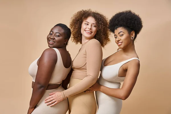 Smiling body positive multiracial women in underwear posing on beige backdrop, plus size charm — Stock Photo