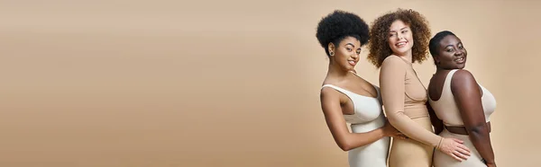 Smiling body positive multiracial women in underwear posing on beige backdrop, horizontal banner — Stock Photo