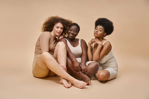 Longueur totale de multiculturel plus la taille des copines en sous-vêtements assis sur beige, expression de soi — Photo de stock