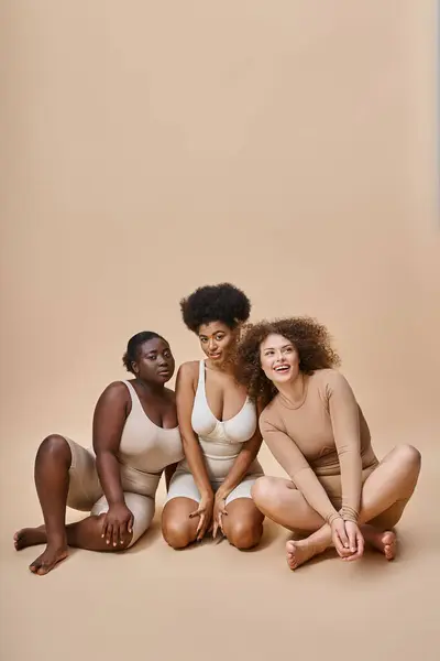Trois joyeux multiracial plus la taille des femmes en sous-vêtements assis sur beige, corps naturel beauté positive — Photo de stock