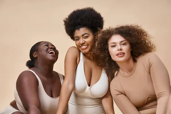 Alegre multirracial más tamaño de las mujeres en ropa interior positivo en beige, belleza natural del cuerpo positivo - foto de stock