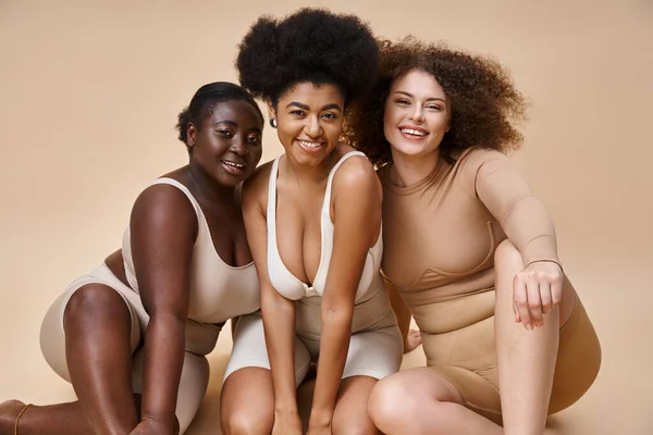Alegre multiétnico plus size mulheres em roupa interior sorrindo em bege, corpo natural beleza positiva — Fotografia de Stock