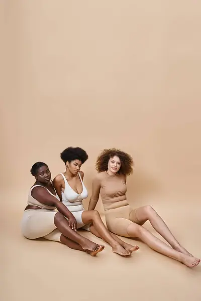 Charmante multiethnische Frauen in Unterwäsche sitzen auf grauem Hintergrund, natürliche plus size Schönheit — Stock Photo
